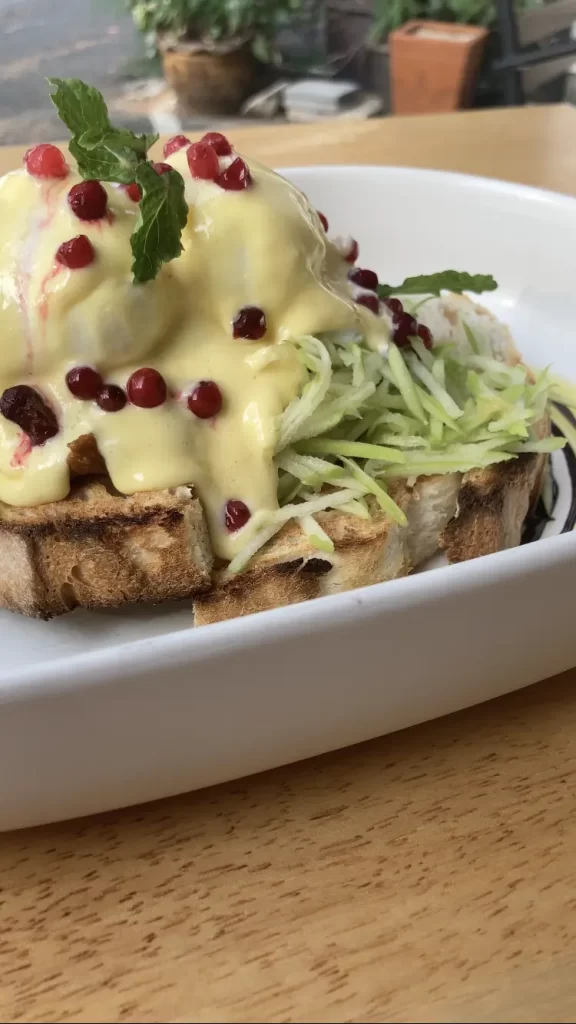 Close up shot of pulled pork eggs benedict with shaved slices of green apple, pomegranate seeds and mint leaves at Poached Breakfast Cafe Rawai Beach, Phuket, Thailand. The best cafe in Nai Harn or Rawai.