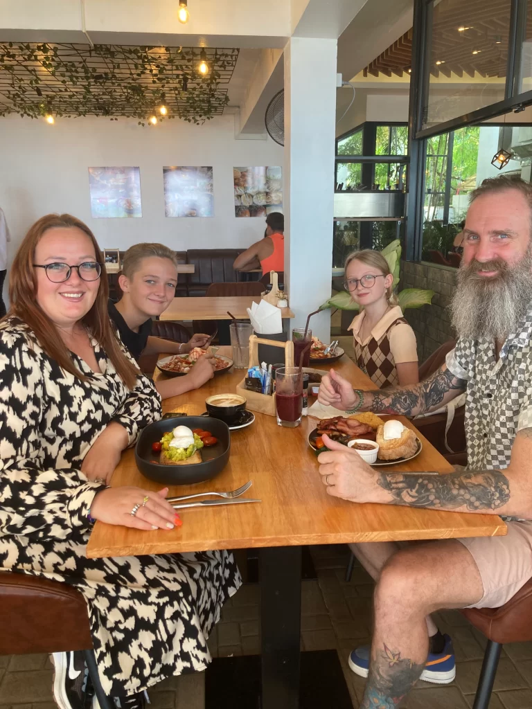 Happy family smiling at the camera with their meals in front of them at Poached Rawai Beach, Phuket, Thailand. Breakfast near Rawai.