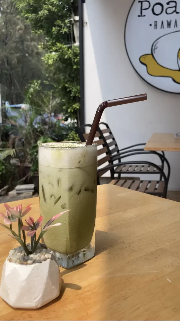 Iced Matcha Tea with a straw, on a table in the sunshine. Just one of the healthy options in Rawai at Poached Rawai Beach, Phuket, Thailand.