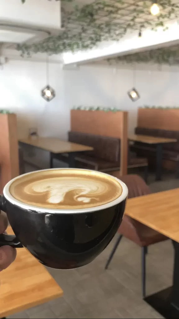 A person holding a latte in the interior of Poached Breakfast Cafe, one of the best breakfast spots in Rawai, Phuket, Thailand