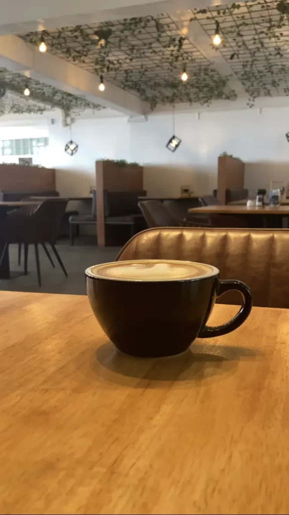 A latte on the table, with some booths in the background of Poached Breakfast Cafe Rawai Beach, Phuket, Thailand. The best coffee in Rawai.