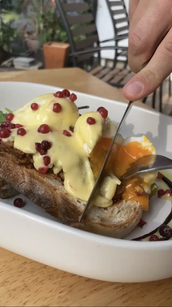 Someone cutting into some perfectly cooked poached eggs covered with hollandaise sauce and pomegranate seeds at the best coffehouse in Rawai: Poached Breakfast near Rawai Beach, Phuket, Thailand