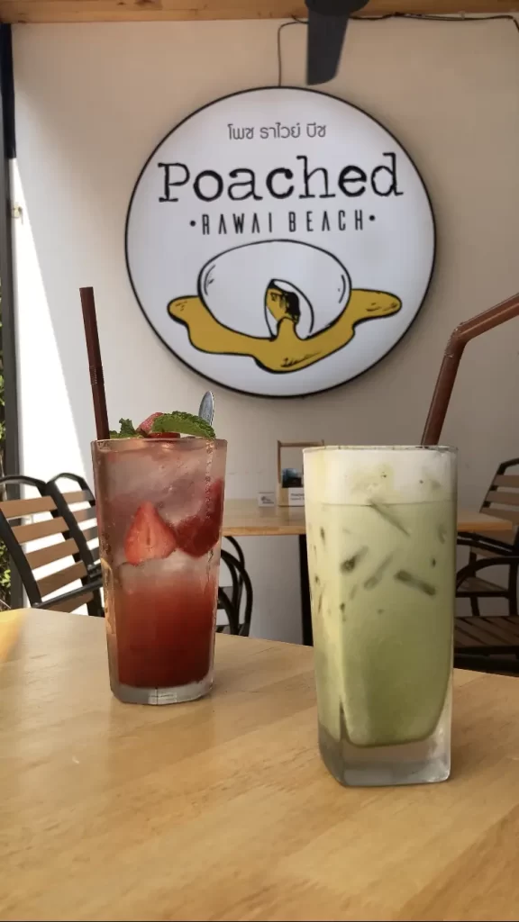 An iced matcha latte with a straw, next to a strawberry flavoured Italian soda in the sunshine on the patio of Poached Breakfast Cafe Rawai Beach, Phuket, Thailand