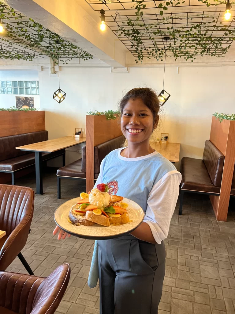 Staff member holding a plate stacked with french toast, bananas, strawberries, ice cream and mint leaves at one of the best places to eat in Rawai: Poached Breakfast Cafe, Rawai, Phuket, Thailand