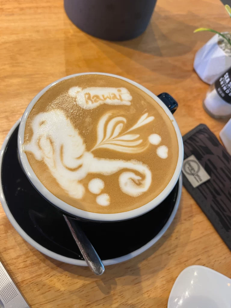 Intricate latte art spelling out Rawai next to a swirling design at Poached Breakfast Cafe, Rawai, Phuket, Thailand. The best takeout coffee in Rawai.