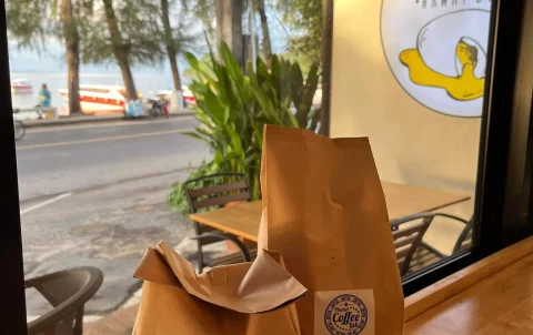 Two bags of coffee beans on a wooden table next to a window overlooking the ocean at Poached Breakfast Cafe Rawai, Phuket, Thailand