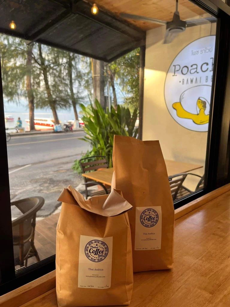 Two bags of coffee beans on a wooden table next to a window overlooking the ocean at Poached Breakfast Cafe Rawai, Phuket, Thailand