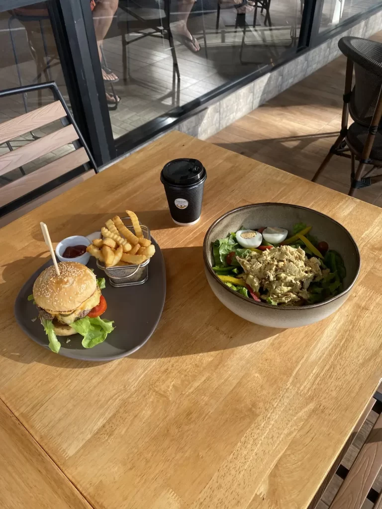 Burger and salad outside on the table at the spot that answers the question, 'What to eat in Nai Harn?'  Poached Breakfast Cafe Rawai, Phuket, Thailand