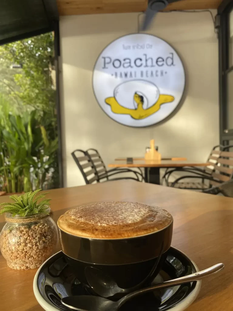 A cappuccino in the morning light on a table at the beachfront of Rawai. One of the best things to do in Rawai at Poached Breakfast Cafe Rawai, Phuket, Thailand