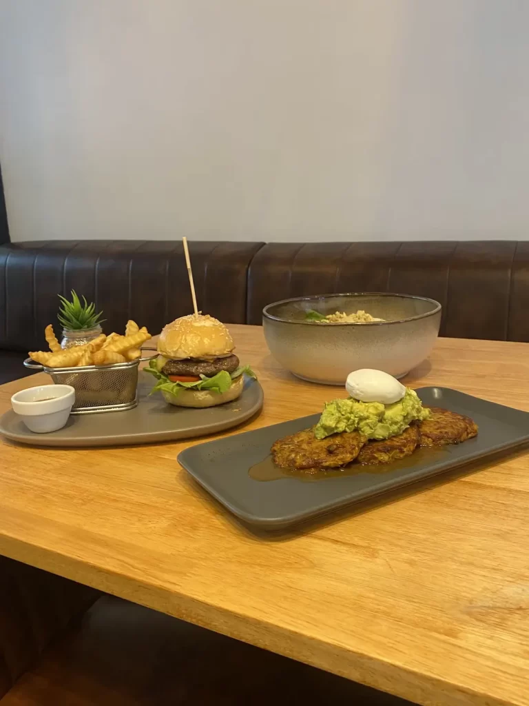 Burger and fries on a table, zucchini fritters with smashed avo and a poached egg and a curried egg salad. Only at Poached Breakfast Cafe Rawai, Phuket, Thailand - the best Western breakfast in Rawai!