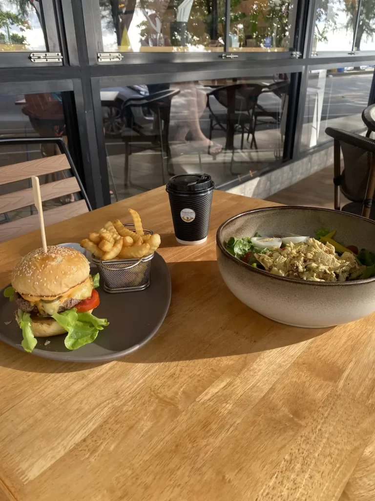 Burger and fries with a salad on a table at the answer to the question, where to go in Nai Harn: Poached Breakfast Cafe Rawai, Phuket, Thailand