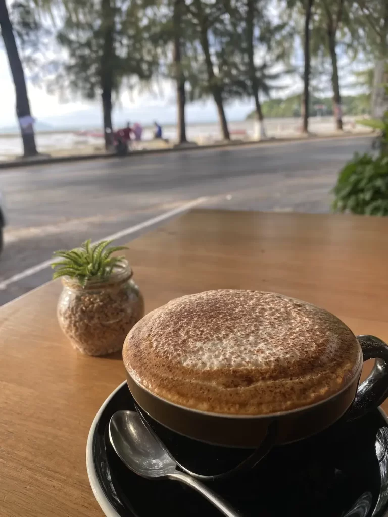 A cappuccino with a view of the beach at the answer to the question, where to go in Nai Harn: Poached Breakfast Cafe Rawai, Phuket, Thailand