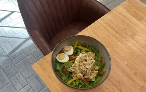 Chicken curry salad topped with a boiled egg on a table, next to two comfortable tub chairs at the spot that serves the best breakfast in Nai Harn: Poached Breakfast Cafe Rawai, Phuket, Thailand