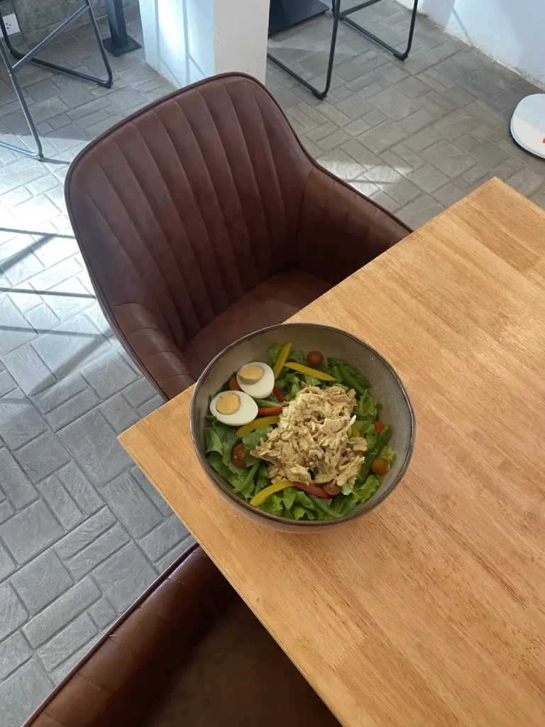 Chicken curry salad topped with a boiled egg on a table, next to two comfortable tub chairs at the spot that serves the best breakfast in Nai Harn: Poached Breakfast Cafe Rawai, Phuket, Thailand