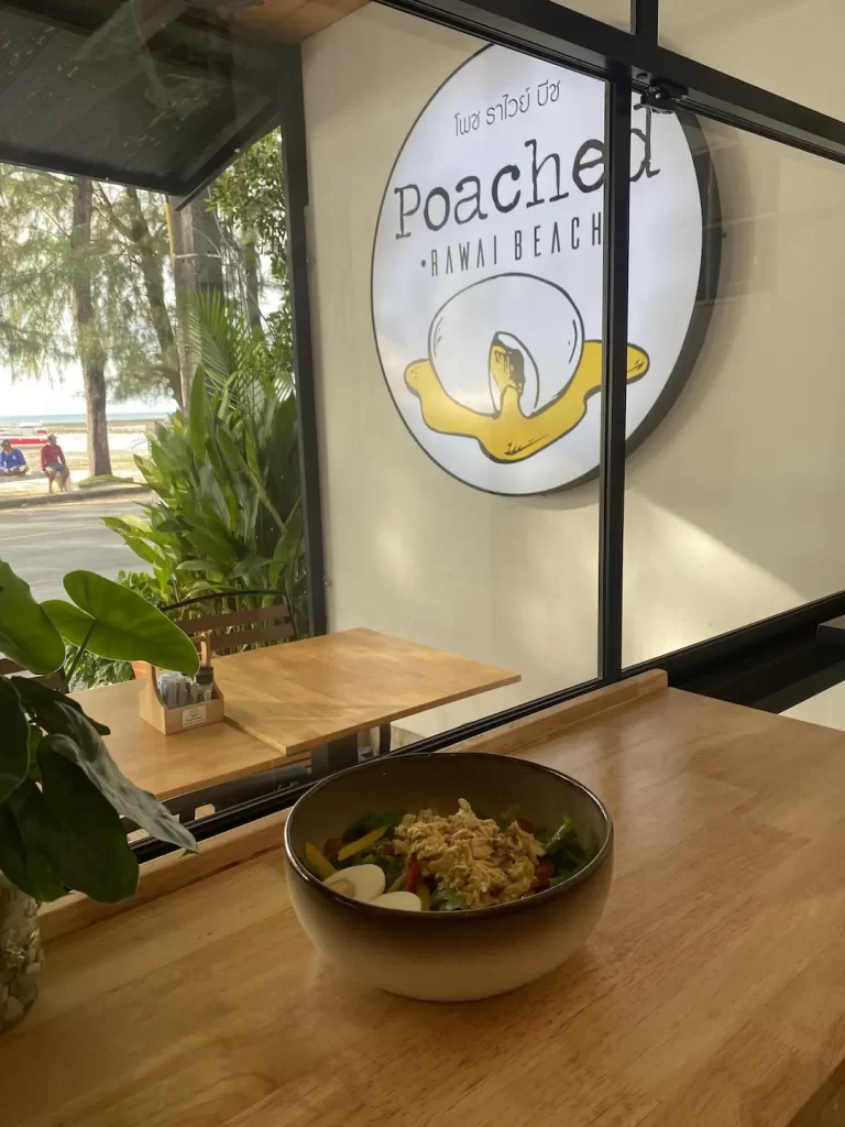 Curried chicken salad on a table with a view of the Poached Breakfast Cafe logo and the ocean at one of the best tourist attractions in Naiharn at Poached Breakfast Cafe Rawai, Phuket, Thailand