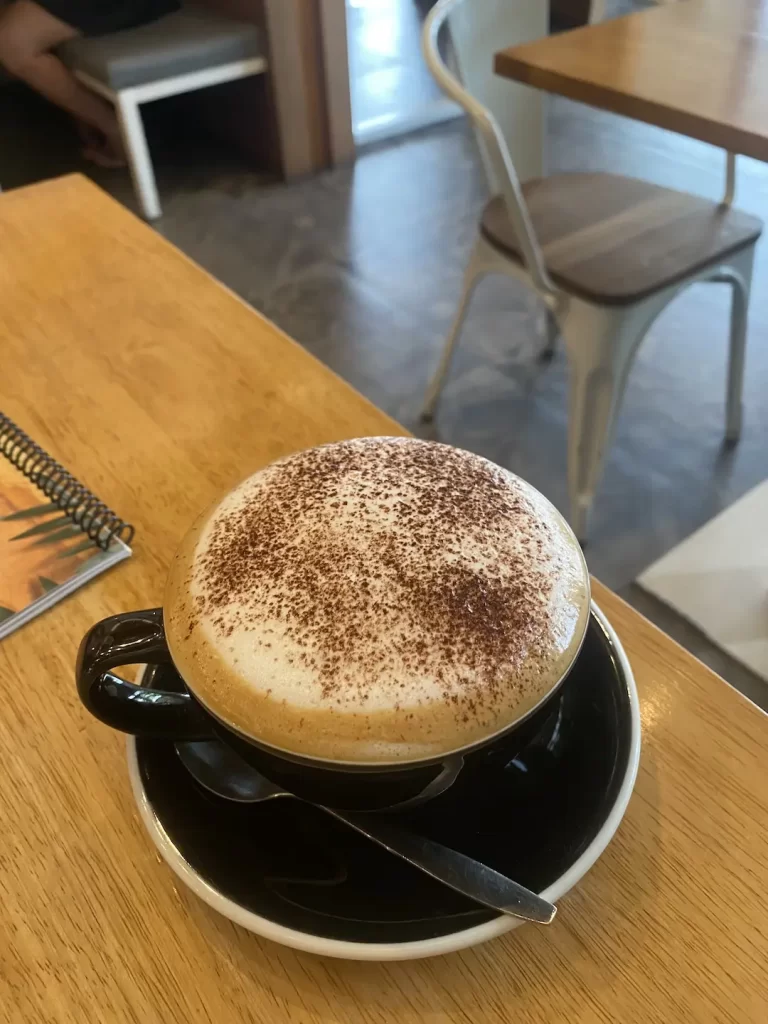 A frothy cappuccino topped with chocolate powder in a large mug on the table at the spot that serves the best breakfast in Nai Harn: Poached Breakfast Cafe Rawai, Phuket, Thailand