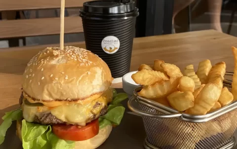 Juicy burger with 2 types of melty cheese, jalapenos, lettuce and tomato next to a basket of crispy crinkle fries and a take away coffee. Only at Poached Breakfast Cafe Rawai, Phuket, Thailand - the best Western breakfast in Rawai!