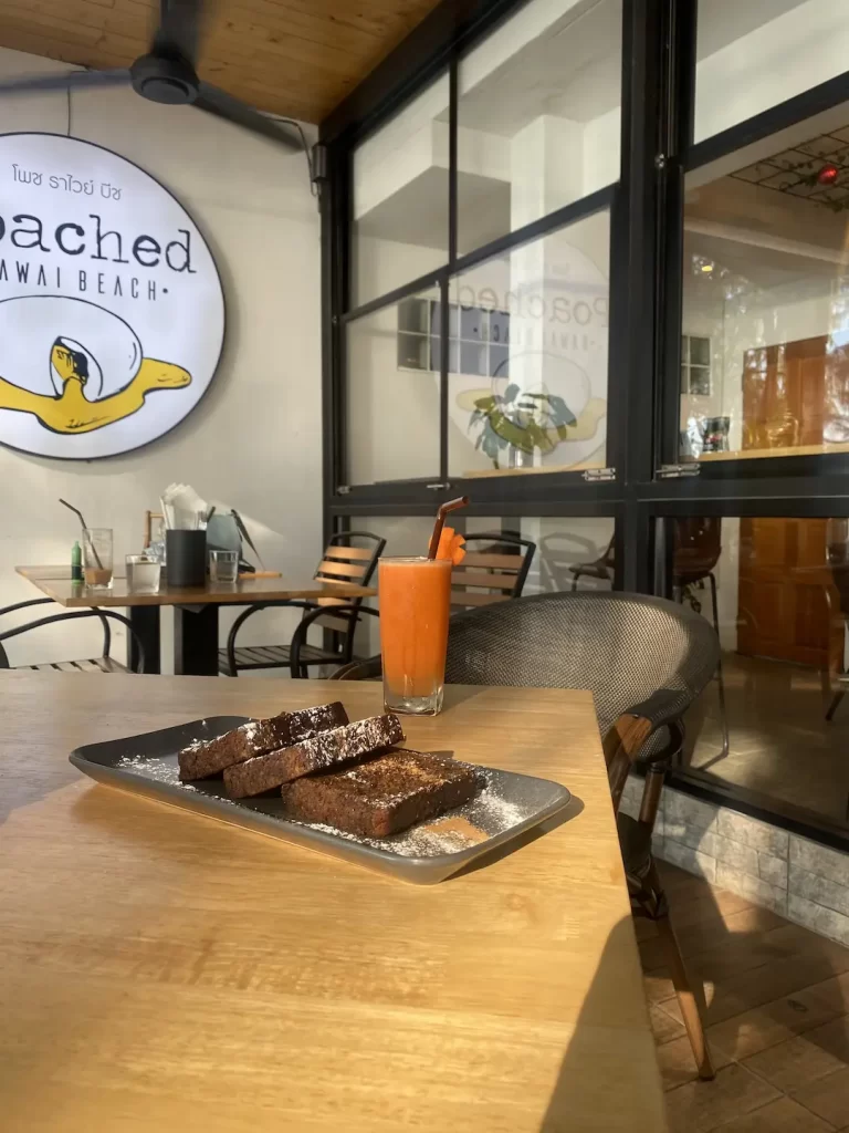 Banana bread on a table with a delicious carrot juice and the Poached sign in the background. This is the best spot for a yummy Nai Harn brunch: Poached Breakfast Cafe Rawai, Phuket, Thailand