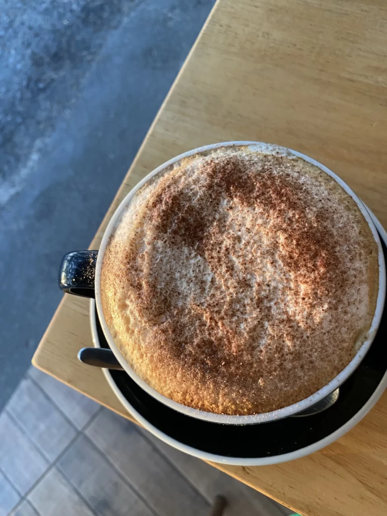 Frothy cappuccino on the corner of a table at Poached Breakfast Cafe Rawai, Phuket Thailand. The perfect drink to fuel you up before you hit up one of the Muay Thai gyms in Rawai.