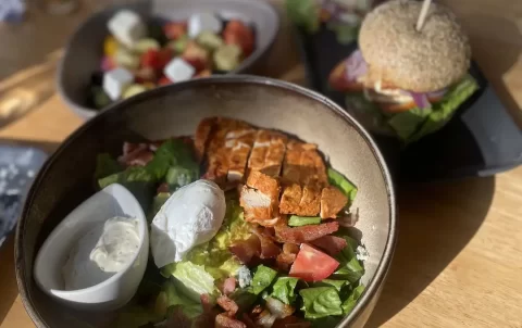 Cobb Salad with ranch dressing and a poached egg in the foreground. In the background you can see a blurry image of a greek salad and a bagel. This is the best spot for a yummy Nai Harn brunch: Poached Breakfast Cafe Rawai, Phuket, Thailand