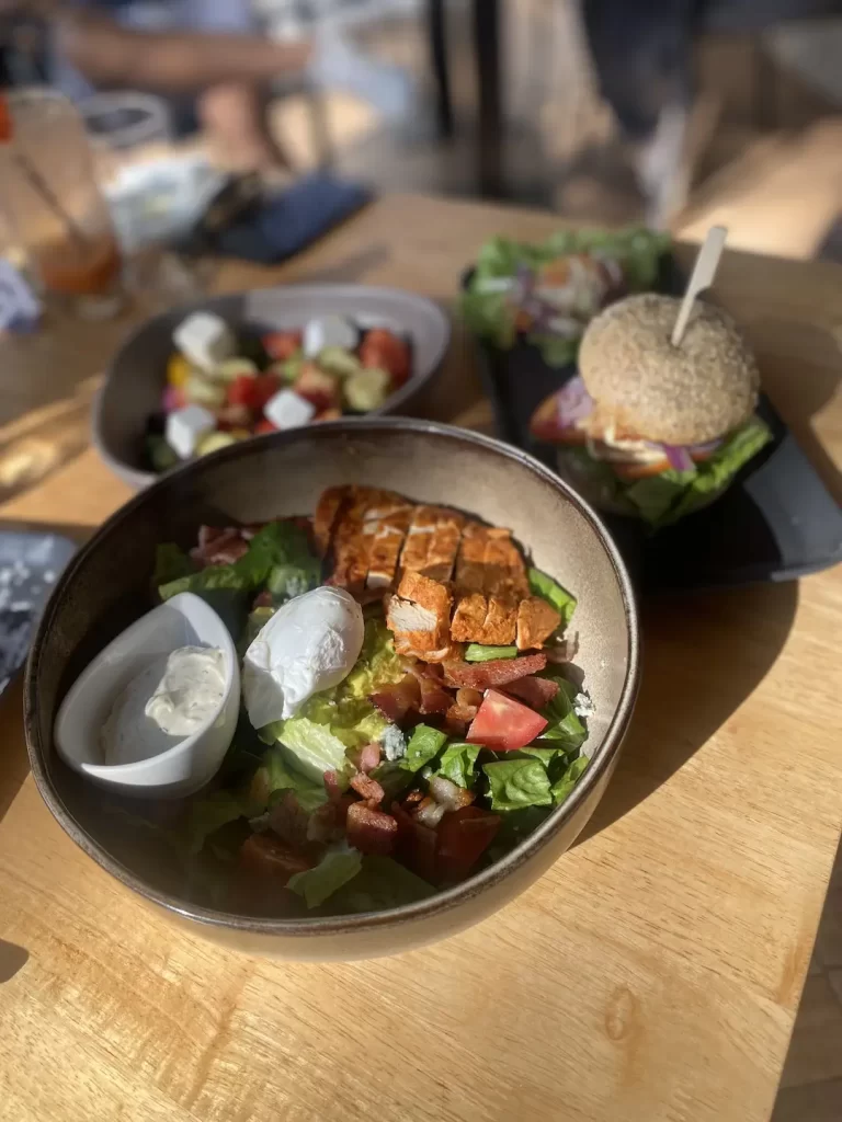 Cobb Salad with ranch dressing and a poached egg in the foreground. In the background you can see a blurry image of a greek salad and a bagel. This is the best spot for a yummy Nai Harn brunch: Poached Breakfast Cafe Rawai, Phuket, Thailand