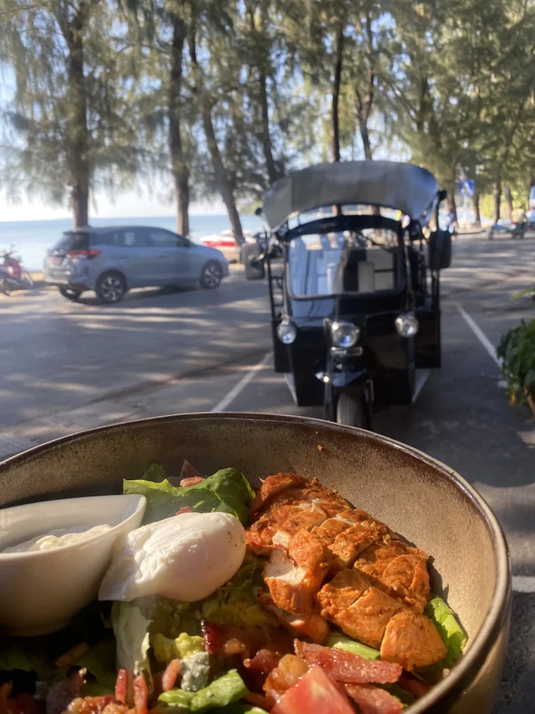 Delicious Cobb Salad with fresh grilled chicken, blue cheese, a poached egg and ranch dressing in front of the Rawai beachfront and a local tuk tuk. All this at the best place to start when you're wanting to explore the walking routes in Rawai: Poached Breakfast Cafe Rawai, Phuket, Thailand