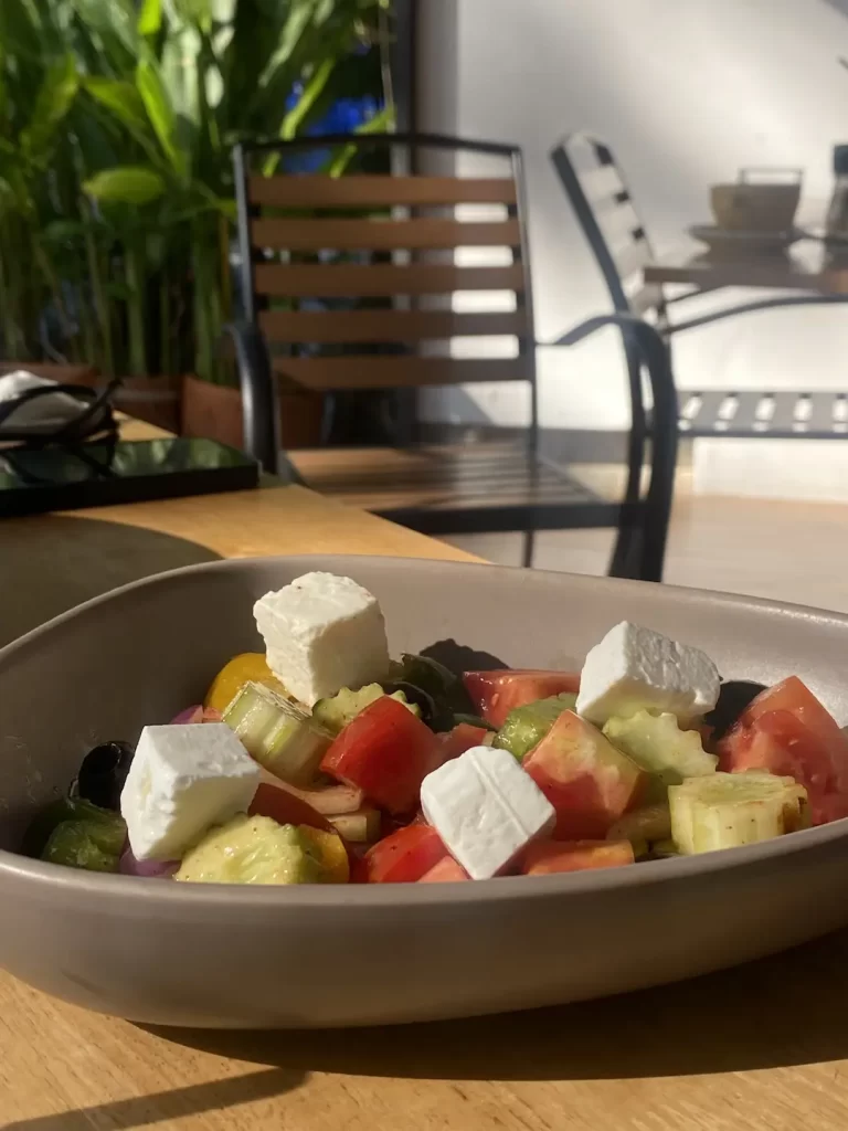 Close up of a greek salad outdoors with sun shining on the table. This is the best spot for a yummy Nai Harn brunch: Poached Breakfast Cafe Rawai, Phuket, Thailand