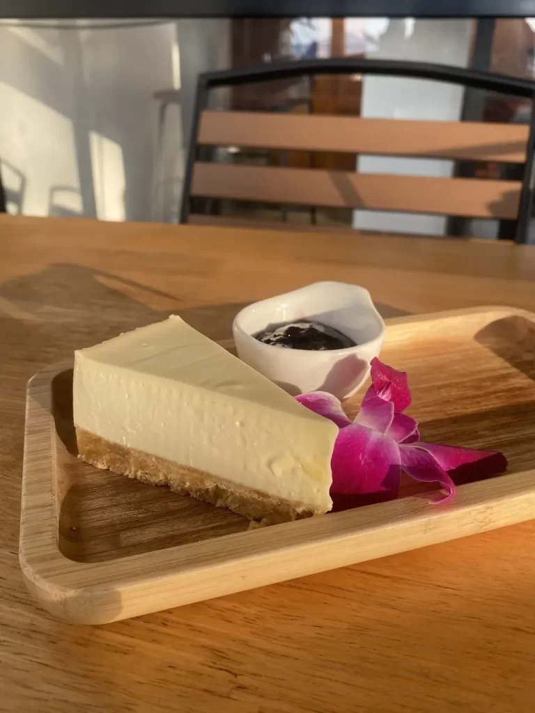 Cheesecake with blueberry jam on a table outdoors. This makes for the perfect treat before you head off to a beach club in Rawai. Only at Poached Breakfast Cafe Rawai, Phuket, Thailand.