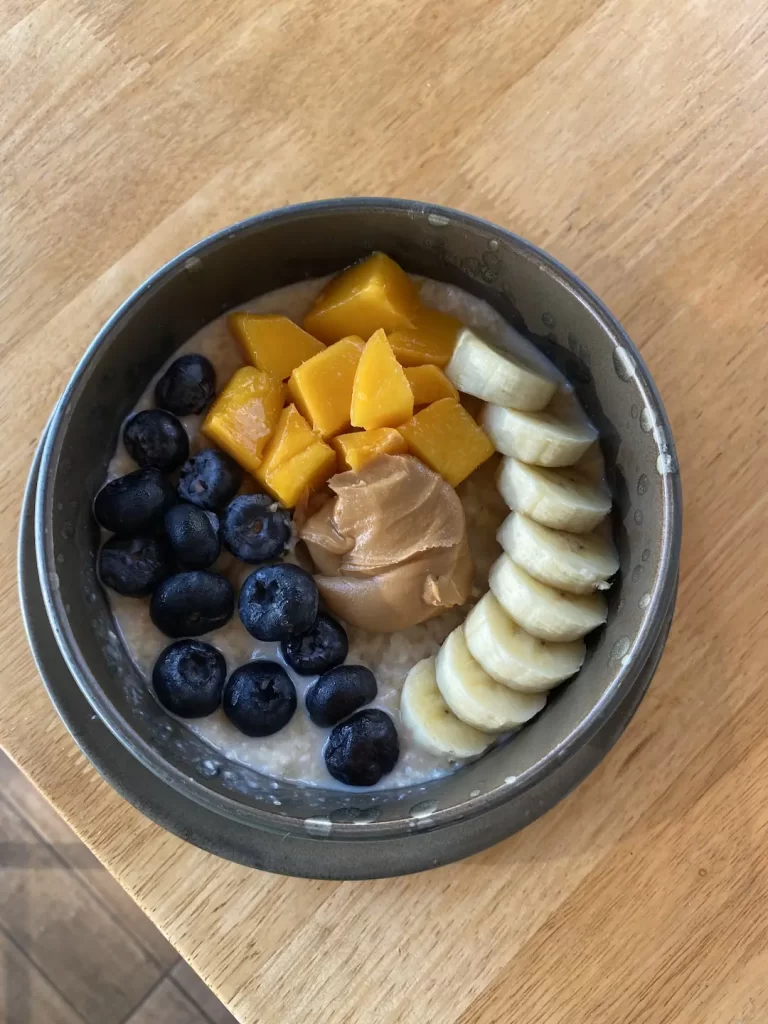 Vegan porridge bowl topped with peanut butter, banana, mangoes and berries at the place with the best cafe culture in Nai Harn: Poached Breakfast Cafe Rawai, Phuket, Thailand