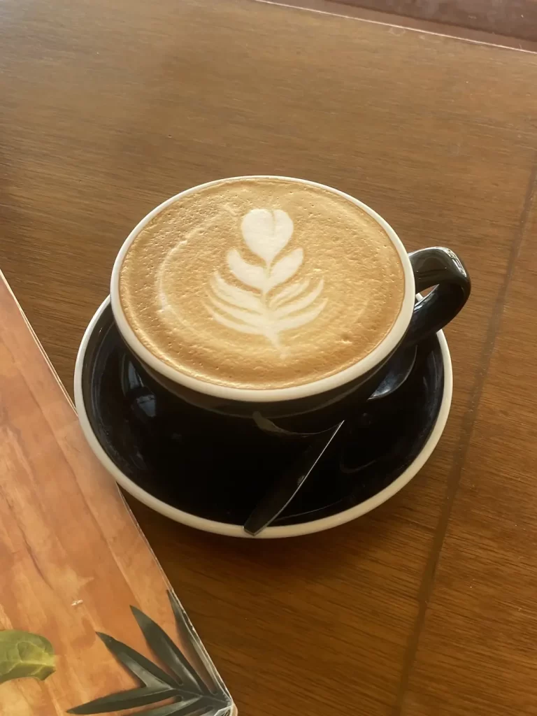 A latte in a large cup with a leaf made with foam in the top. We serve the best specialty coffee in Rawai at Poached Breakfast Cafe, Rawai, Phuket, Thailand