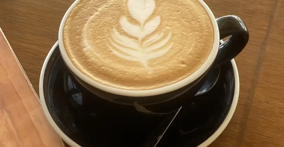 A latte in a large cup with a leaf made with foam in the top. We serve the best specialty coffee in Rawai at Poached Breakfast Cafe, Rawai, Phuket, Thailand