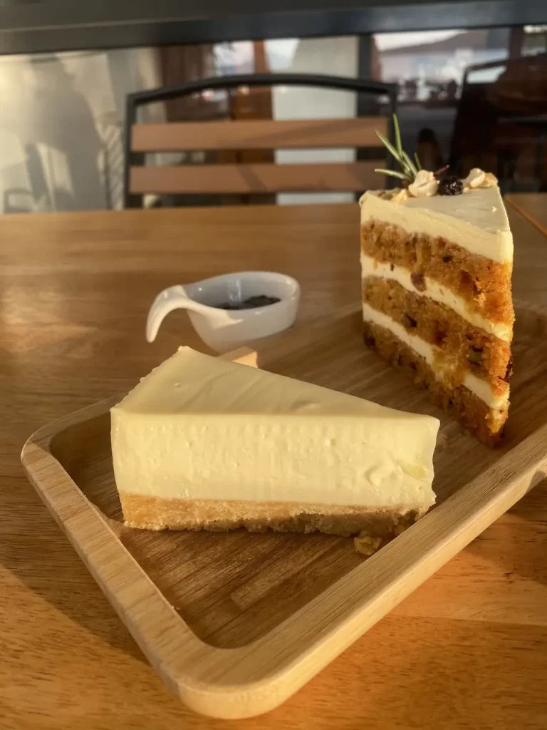 Cheese cake and a carrot cake slice on a wooden platter. Only at the spot with the best caesar salad near Nai Harn, Poached Breakfast Cafe Rawai, Phuket, Thailand