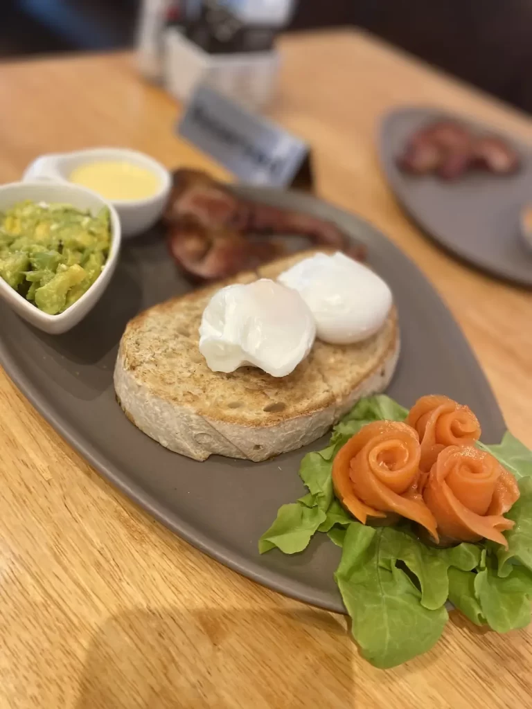 A plate with smoked salmon, sourdough bread, crispy canadian bacon, two poached eggs, smashed avocado and hollandaise sauce. The most delicious bacon in Nai Harn can be found at Poached Breakfast Cafe Rawai, Phuket, Thailand
