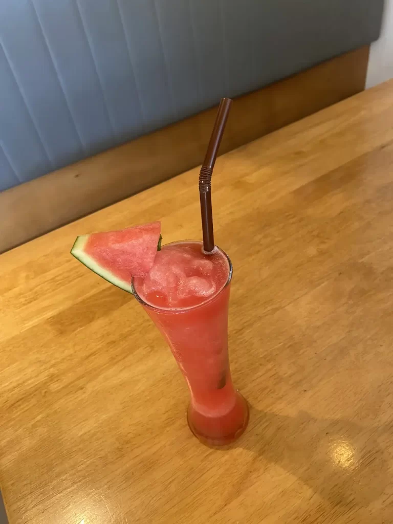 Watermelon smoothie in a tall glass on a wooden table at the spot with the best apple pie near Nai Harn: Poached Breakfast Cafe Rawai, Phuket, Thailand