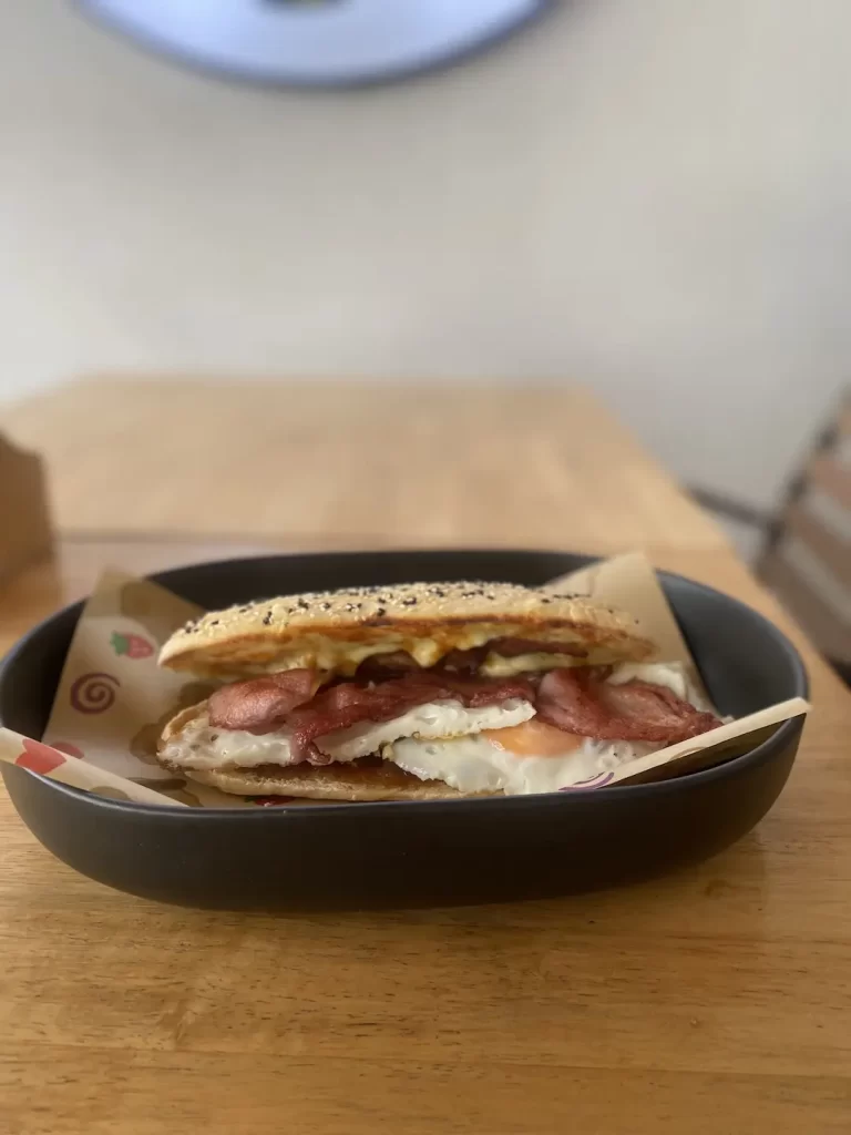 Bacon and egg roll with seeded bun on a table at Poached Breakfast Cafe Rawai, conveniently located near the best resorts near Nai Harn