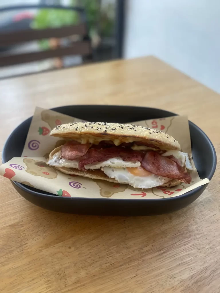 Bacon and egg breakfast sandwich with cheese on a seeded bun. Only at the place with the best coffee menu in Nai Harn: Poached Breakfast Cafe, Rawai, Phuket, Thailand