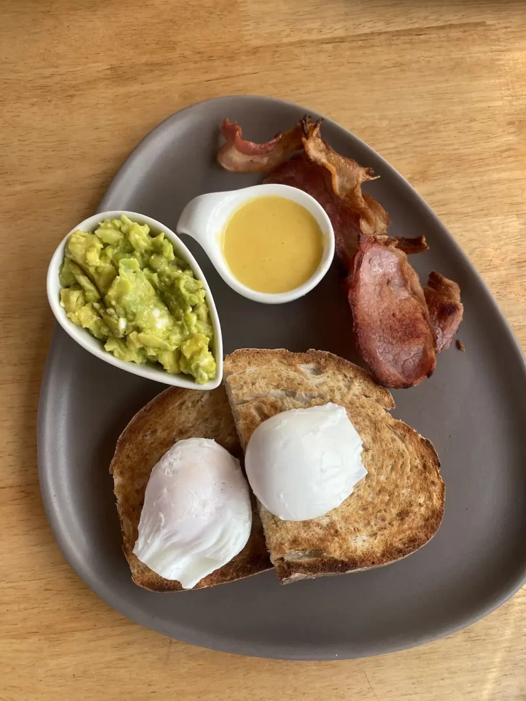 Healthy breakfast with smashed avocado, 2 poached eggs, sourdough bread, hollandaise sauce and lean bacon at the spot to eat at before visiting the best viewpoints near Nai Harn: Poached Breakfast Cafe Rawai, Phuket, Thailand