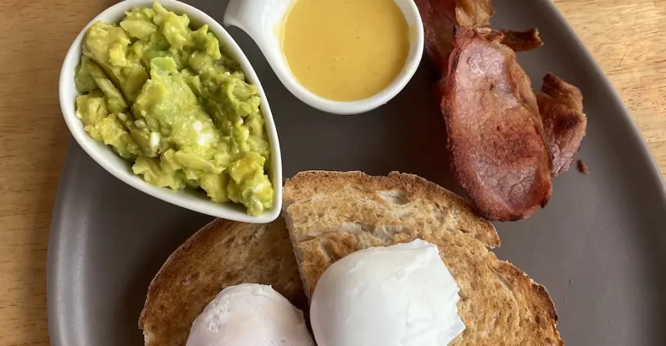 Healthy breakfast with smashed avocado, 2 poached eggs, sourdough bread, hollandaise sauce and lean bacon at the spot to eat at before visiting the best viewpoints in Nai Harn: Poached Breakfast Cafe Rawai, Phuket, Thailand