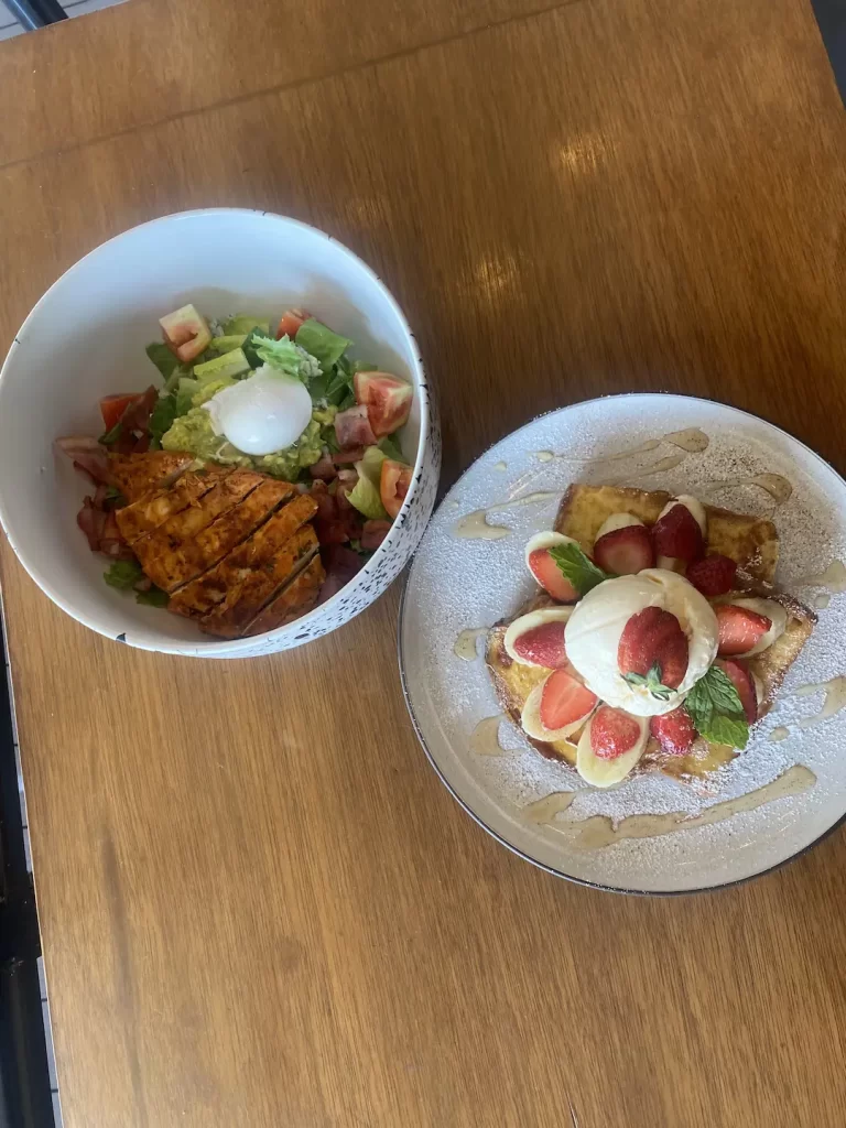 Cobb salad with poached egg, chicken and blue cheese dressing next to a plate of french toast with stacked strawberries, banana and ice cream. All at the best place to eat when you're staying at one of the hostels in Rawai: Poached Breakfast Cafe Rawai, Phuket, Thailand