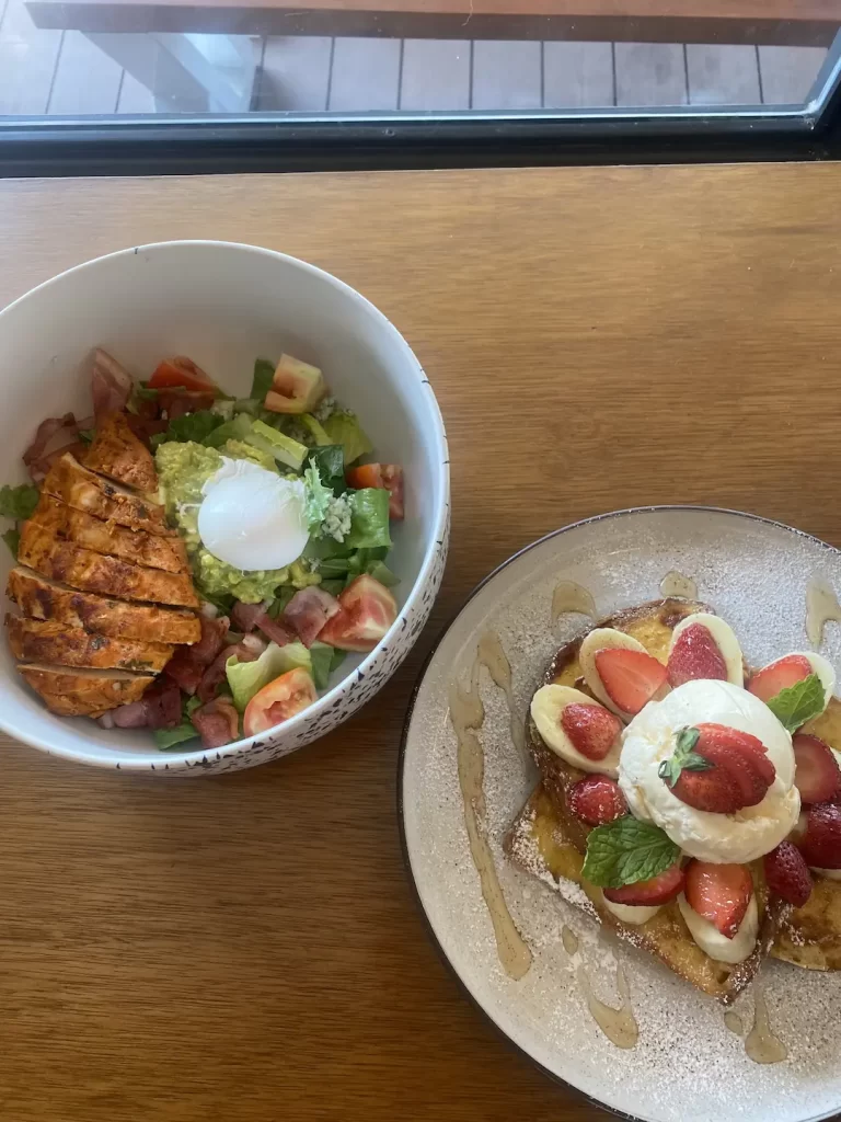 Cobb salad with poached egg next to a plate of french toast topped with banana, strawberries and a scoop of ice cream. Only at the place with the best coffee menu in Nai Harn: Poached Breakfast Cafe, Rawai, Phuket, Thailand