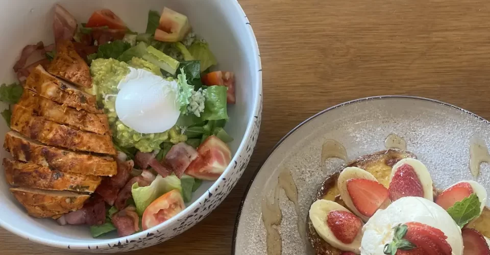 Cobb salad with poached egg next to a plate of french toast topped with banana, strawberries and a scoop of ice cream. Only at the place with the best coffee menu in Nai Harn: Poached Breakfast Cafe, Rawai, Phuket, Thailand