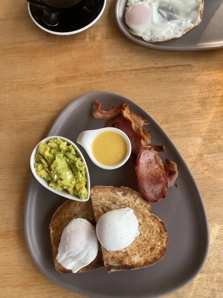 2 poached eggs on sourdough toast with sides of hollandaise sauce, bacon and smashed avocado. A great spot to eat if you're staying at one of the hotels in Rawai. Only at Poached Breakfast Cafe Rawai, Phuket, Thailand