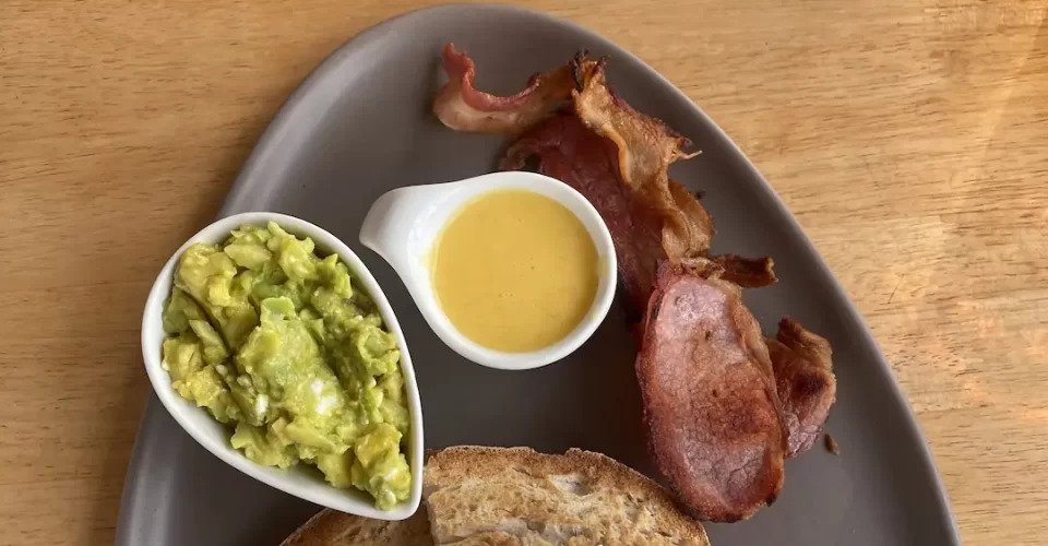 2 poached eggs on sourdough toast with sides of hollandaise sauce, bacon and smashed avocado. A great spot to eat if you're staying at one of the hotels in Rawai. Only at Poached Breakfast Cafe Rawai, Phuket, Thailand